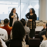 Two people standing in front of an audience that is sitting down.